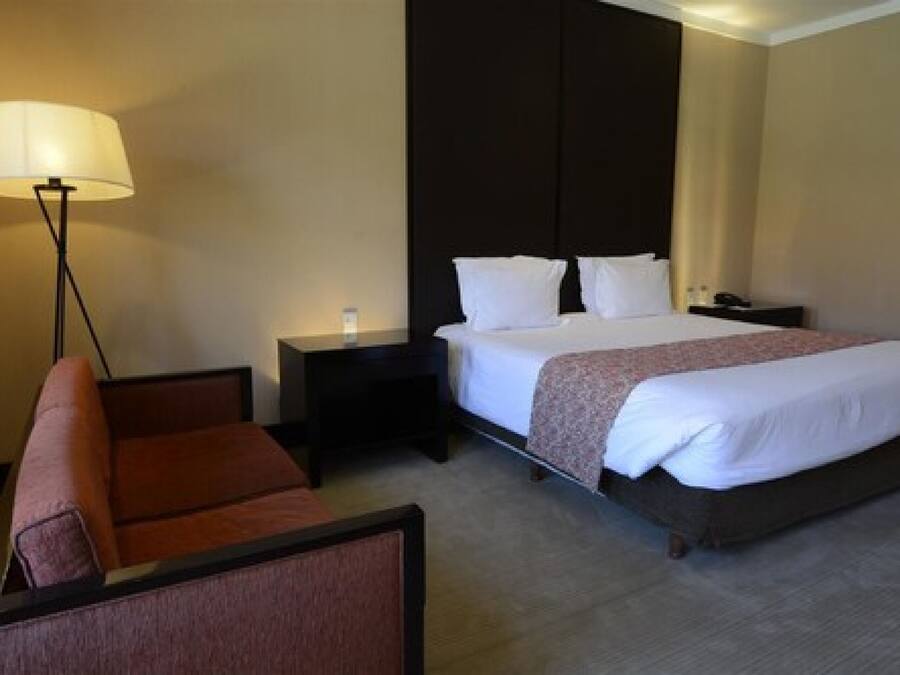 Una habitación de hotel con cama, mesita de noche, lámpara y una silla.
