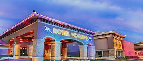 Un hotel con un llamativo letrero de "HOTEL & CASINO", grandes columnas y una entrada bien iluminada.