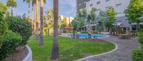 A hotel courtyard with palm trees, a swimming pool, and outdoor seating areas.