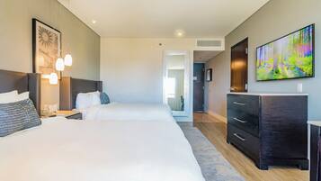 Une chambre d’hôtel moderne avec deux lits, un grand téléviseur à écran plat et une commode en bois foncé.