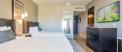 Una habitación de hotel moderna con dos camas, un televisor de pantalla plana grande y un aparador de madera oscura.