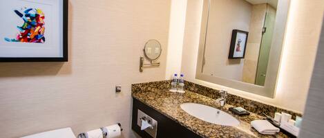 A modern bathroom with a granite countertop, a white sink, a large mirror, and a framed artwork on the wall.