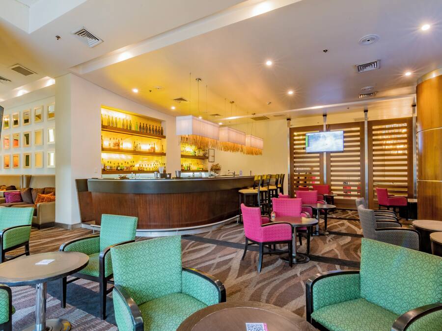 A hotel lobby with a bar area, seating arrangements, and a television screen.