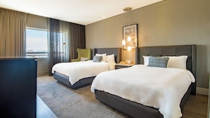 A hotel room with two beds, a desk, and a view of the city.