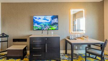 Habitación de hotel con televisor de pantalla plana en la pared, un escritorio con silla, un armario pequeño y una cama.