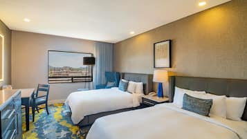 A hotel room with two beds, a desk, a chair, a nightstand, and a window with a view.