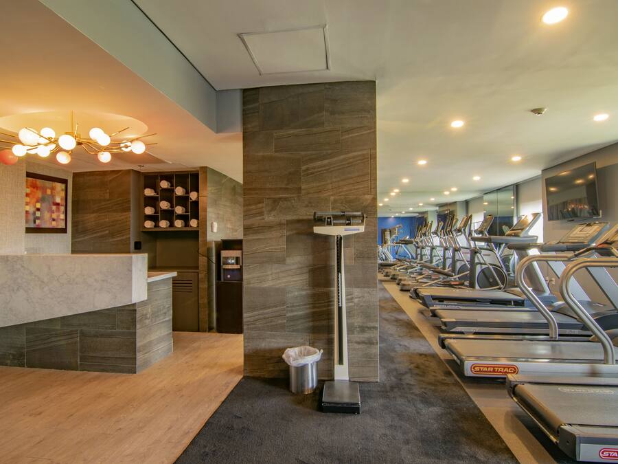 Un gimnasio moderno con una recepción, una báscula y varias cintas de correr.