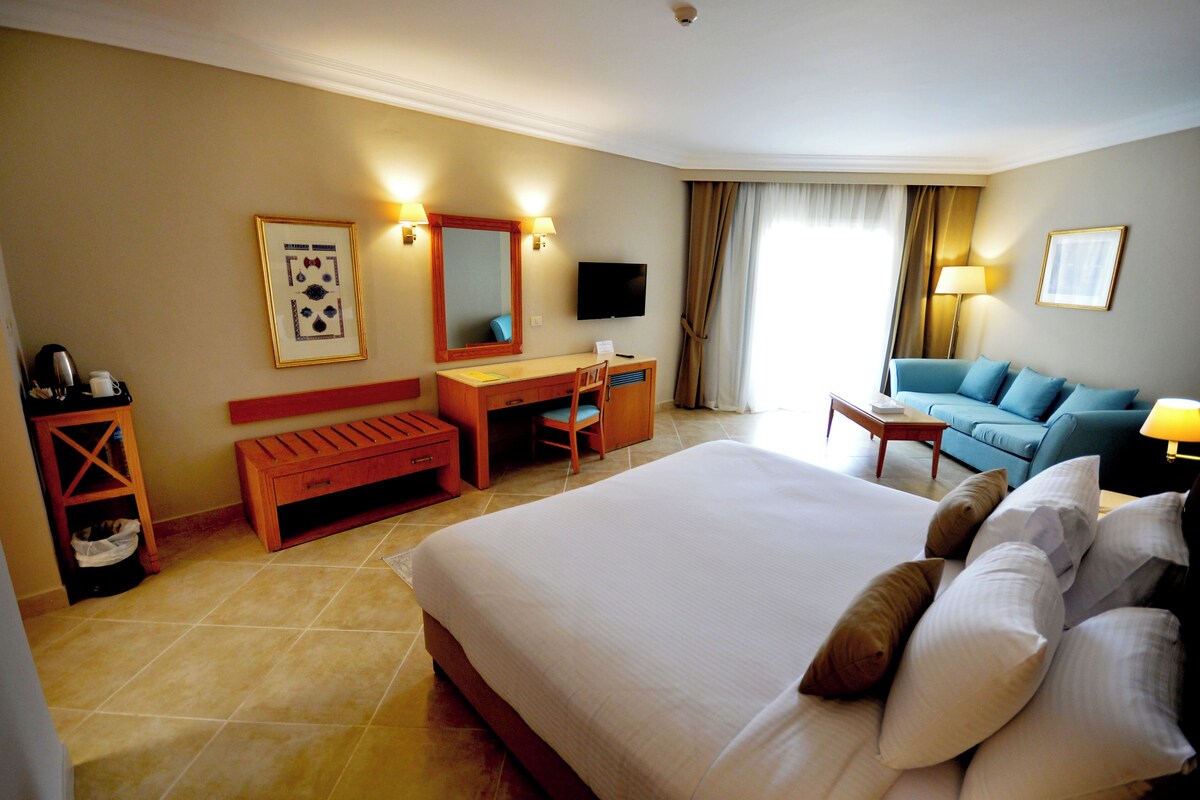Une chambre d’hôtel avec un grand lit, un bureau, une chaise, un canapé et une télévision.