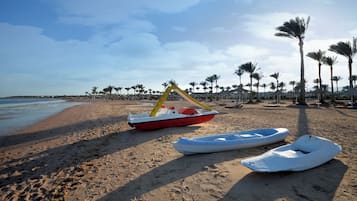 A beach with a row of palm trees, a boat, and a row of beach umbrellas.