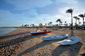 A beach with a row of palm trees, a boat, and a row of beach umbrellas. - Aurora Oriental Resort Sharm El Sheikh (Sharm El Sheikh)