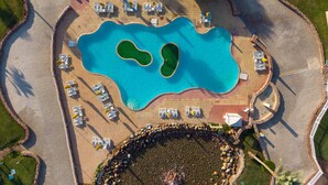 Vue aérienne d’un complexe hôtelier doté d’une grande piscine, de chaises longues et d’un jardin de rocaille circulaire.