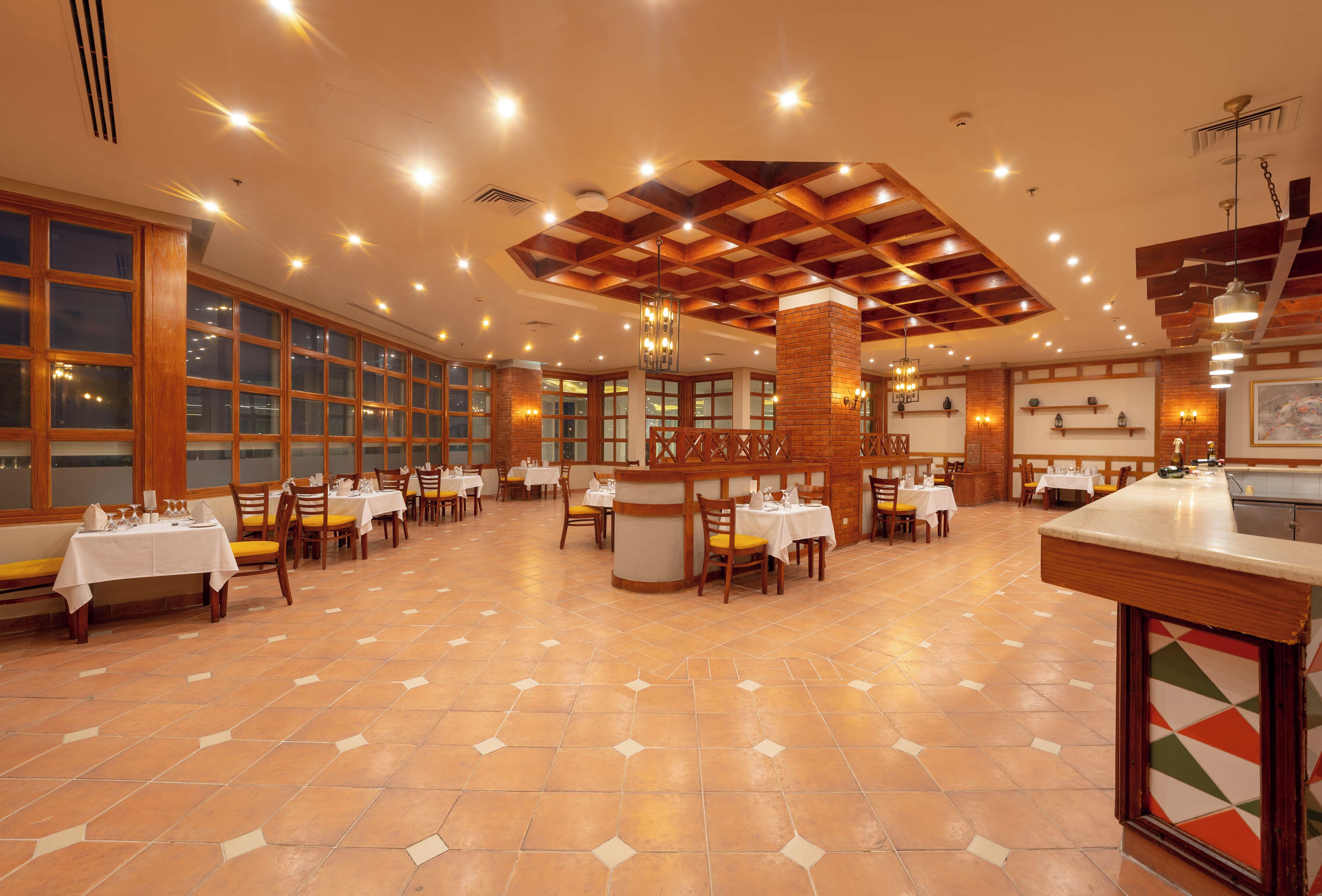 Un restaurant spacieux, doté de nombreuses tables et chaises, d’un plafond haut avec des poutres en bois et de grandes fenêtres.
