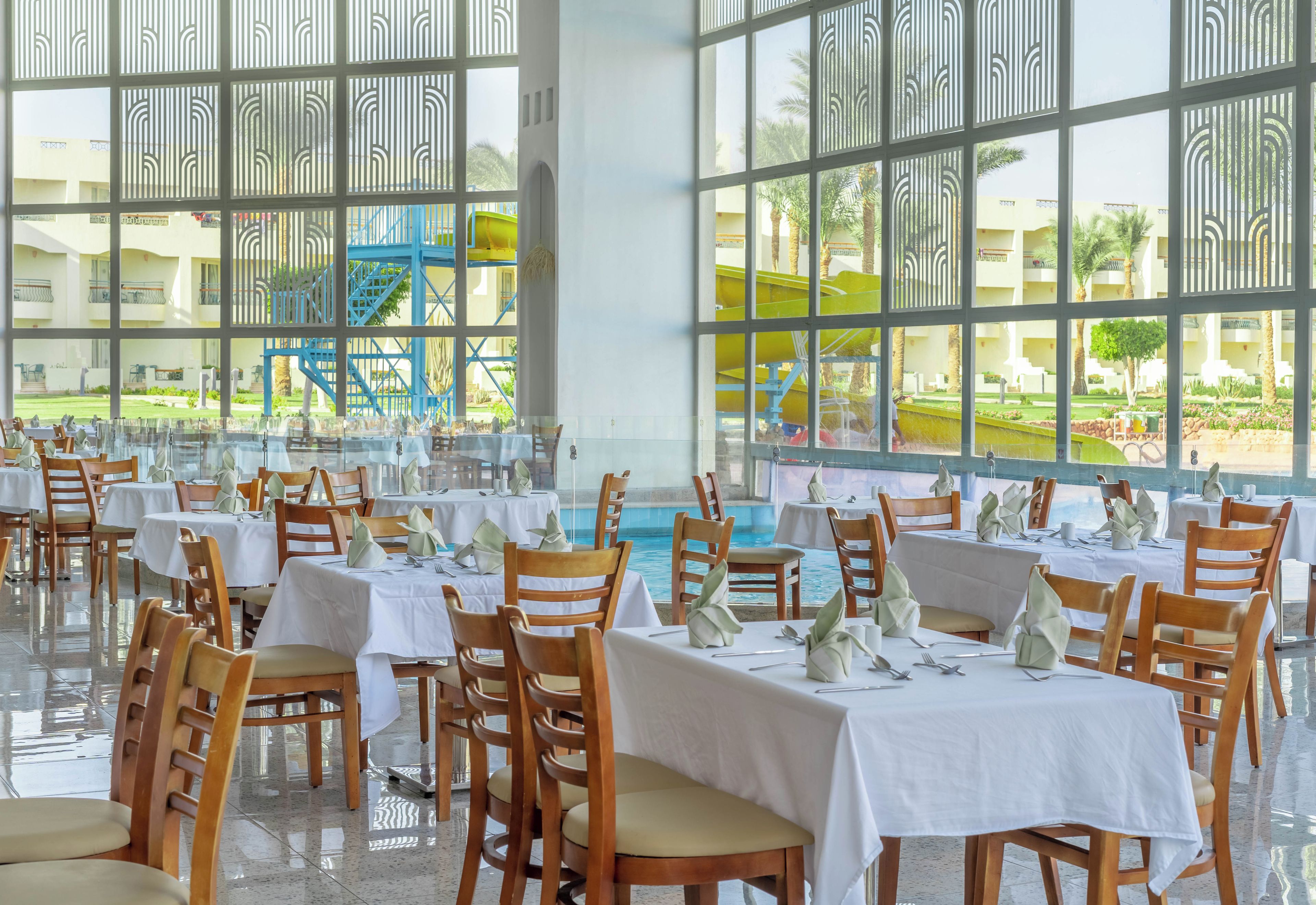 A restaurant with tables set for dining, large windows, and a view of a pool and outdoor area.