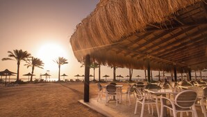 Ein Restaurant direkt am Strand mit Außenbereich, Palmen und einem Reetdach.