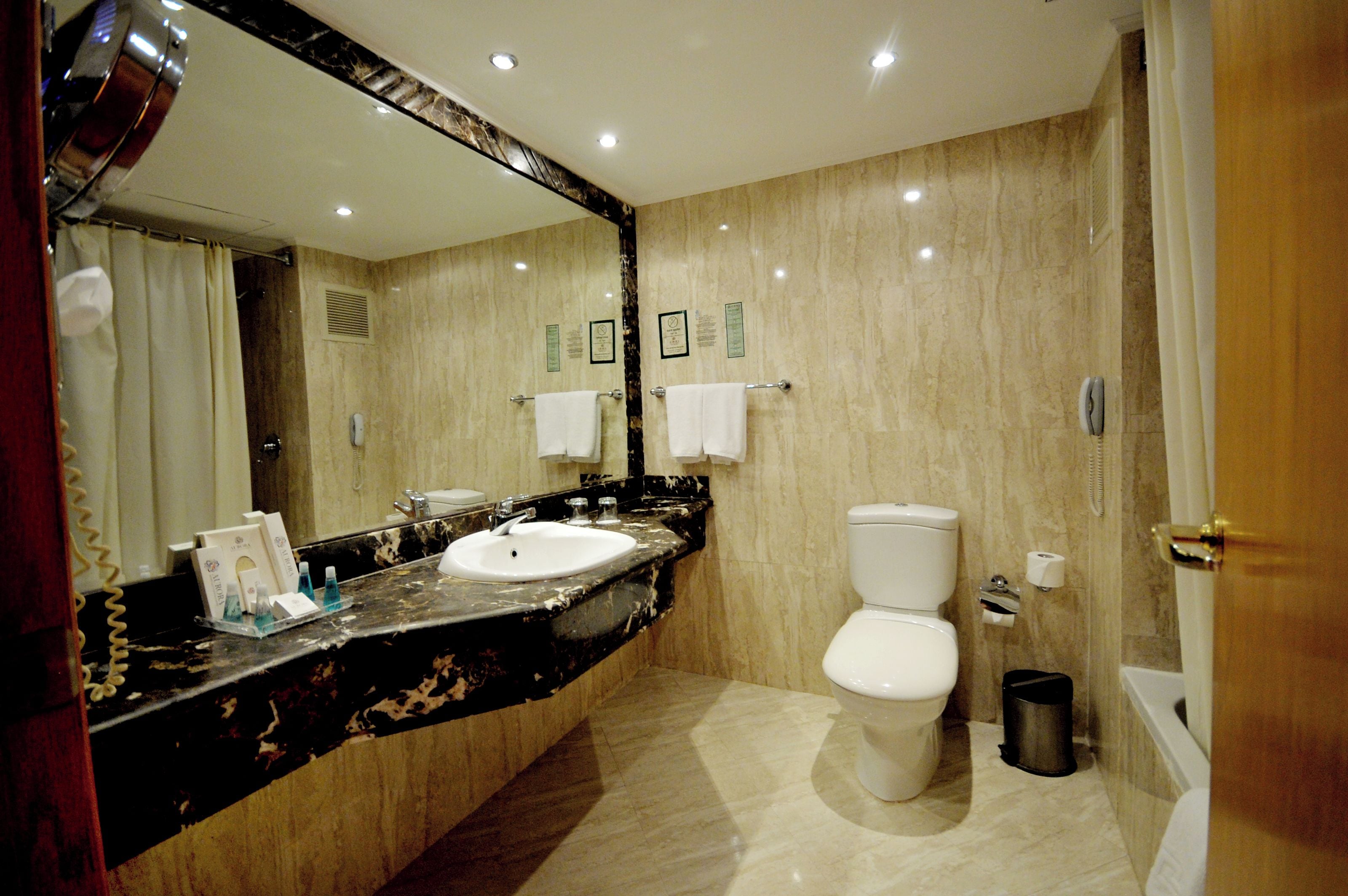 A bathroom with a marble sink, a toilet, and a large mirror.
