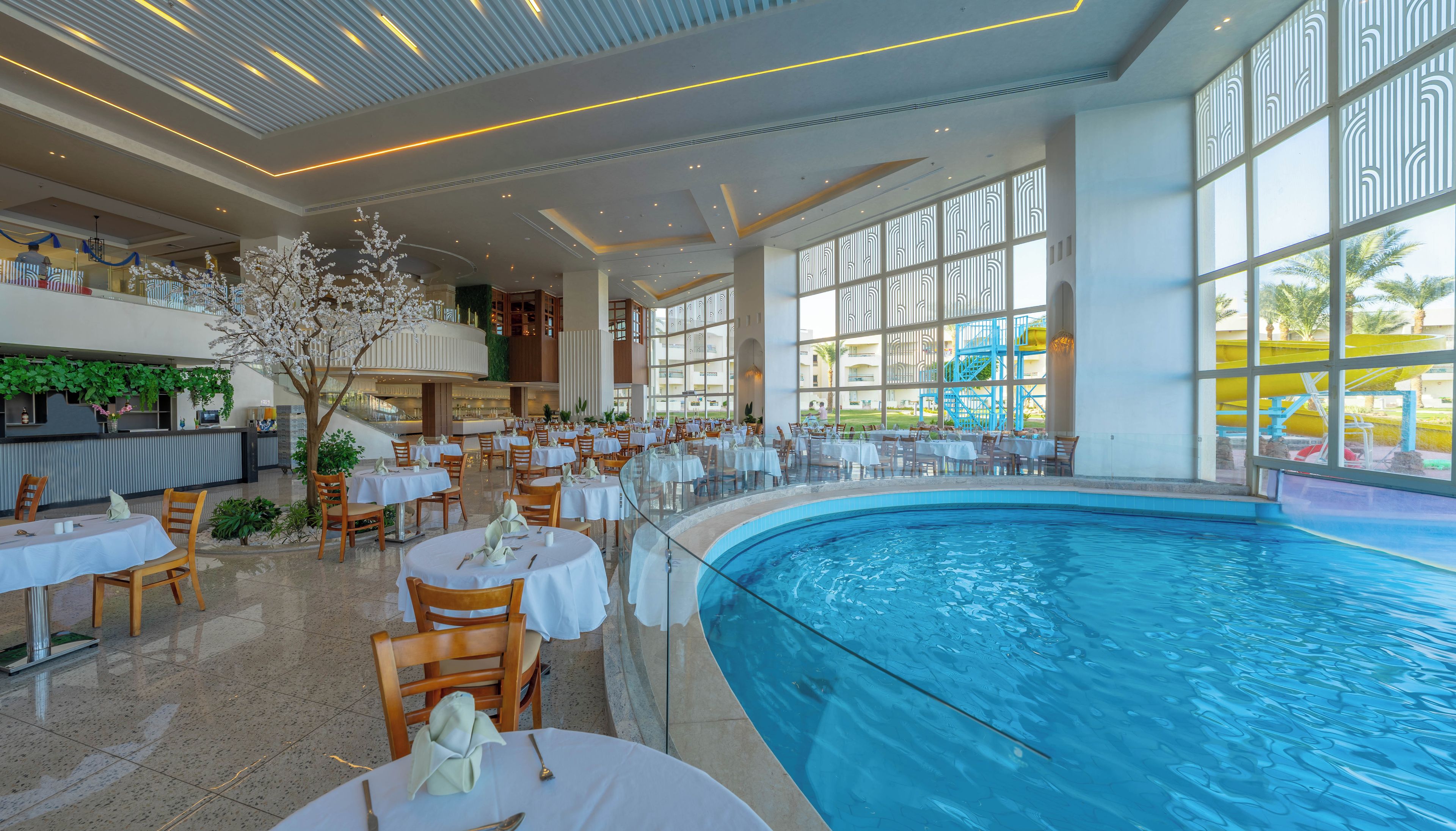 A hotel lobby with a pool, dining area, and large windows.