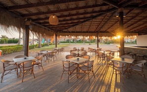 Un espace extérieur aménagé avec des tables et des chaises, un toit de chaume et une vue sur un jardin paysager.