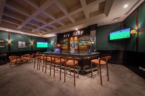 Un espace bar avec un comptoir, des tabourets et un écran de télévision.