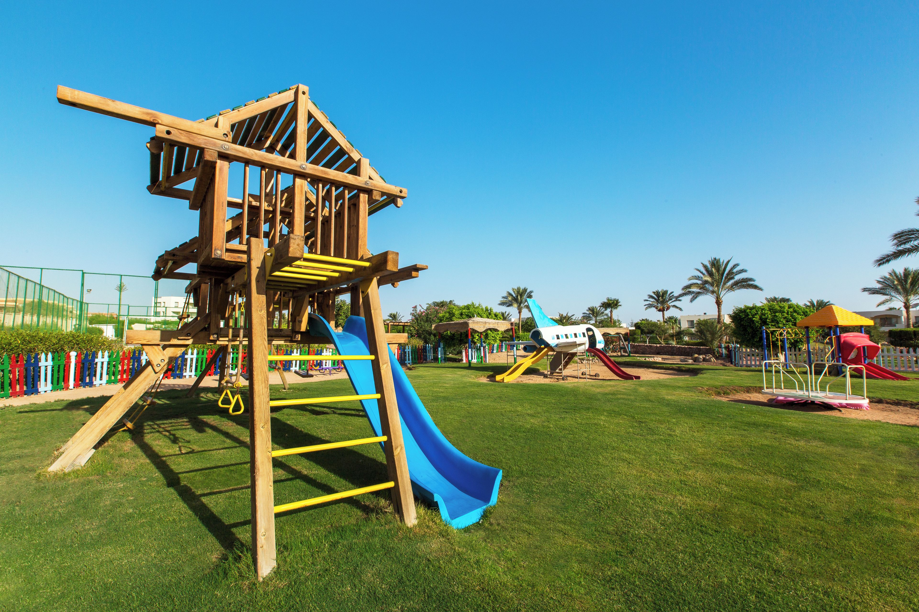 A playground with a wooden climbing structure, slides, and a fenced area.