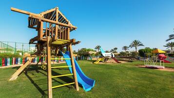 A playground with a wooden climbing structure, slides, and a fenced area.