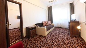 A hotel room with a bed, a desk, a dresser, a lamp, and a patterned carpet. - Hotel Impero (Oradea)