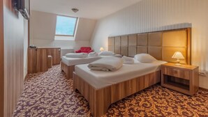 A hotel room with two beds, a red chair, a small desk, and a window. - Hotel Impero (Oradea)
