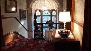 A staircase with a patterned carpet, a wooden chair, a table with a lamp, and a vase of flowers. - Ascot House (York)