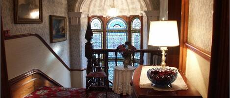 A staircase with a patterned carpet, a wooden chair, a table with a lamp, and a vase of flowers.