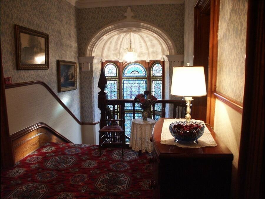 Eine Treppe mit gemustertem Teppich, ein Holzstuhl, ein Tisch mit Lampe und eine Blumenvase.