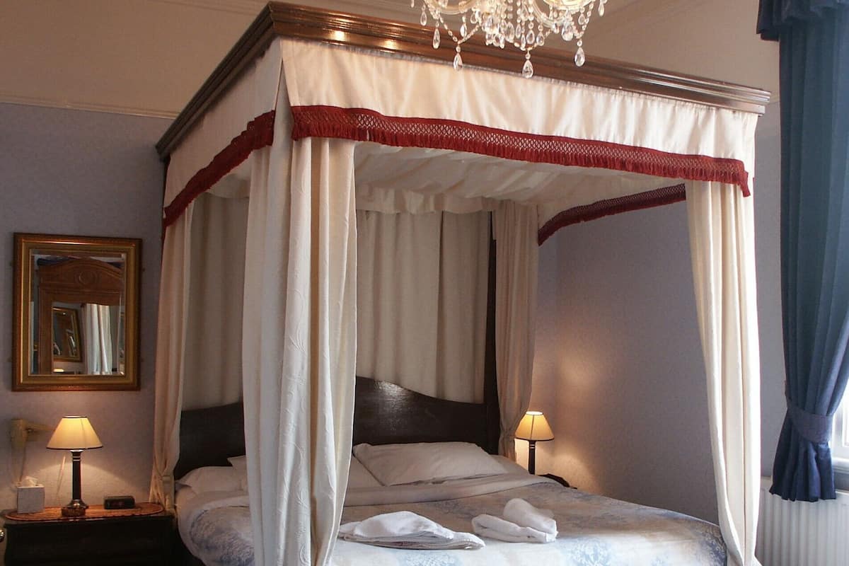 A four-poster bed with a canopy, two bedside lamps, a mirror, and a chandelier.