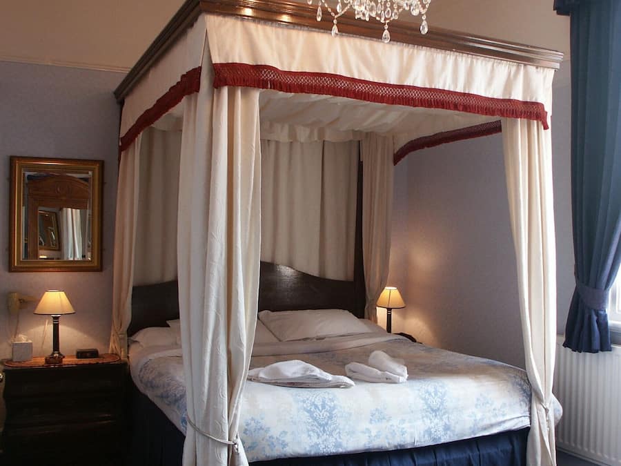 A four-poster bed with a canopy, two bedside lamps, a mirror, and a chandelier.