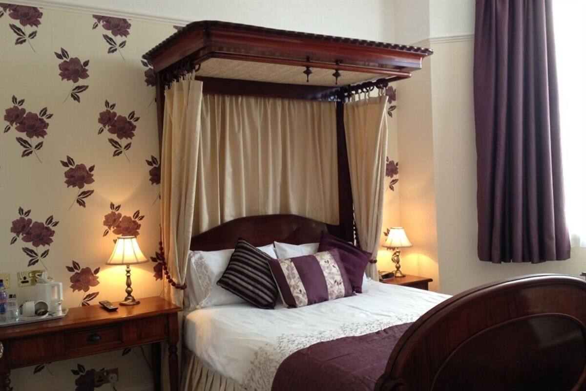 A four-poster bed with a canopy, bedside lamps, a bedside table with a lamp, and a chair.