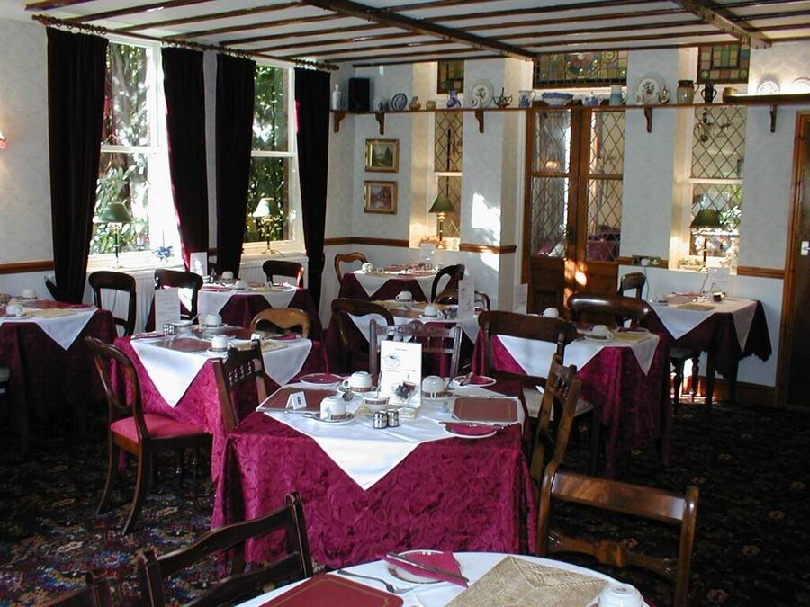 Un espace repas avec plusieurs tables dressées pour le service, des chaises en bois et un tapis à motifs.