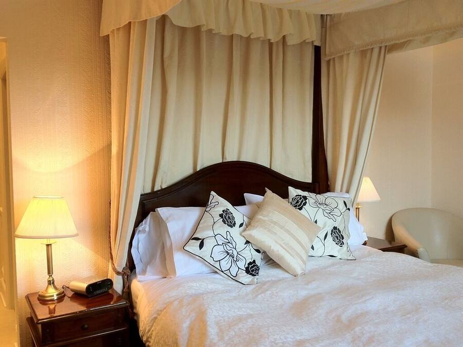 A neatly made bed with floral pillows, a bedside lamp, and a nightstand with a phone and a small device.
