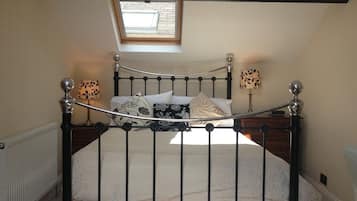 A bedroom with a sloped ceiling, a skylight, a metal bed frame, a white bedspread, two bedside lamps, and a wooden nightstand.