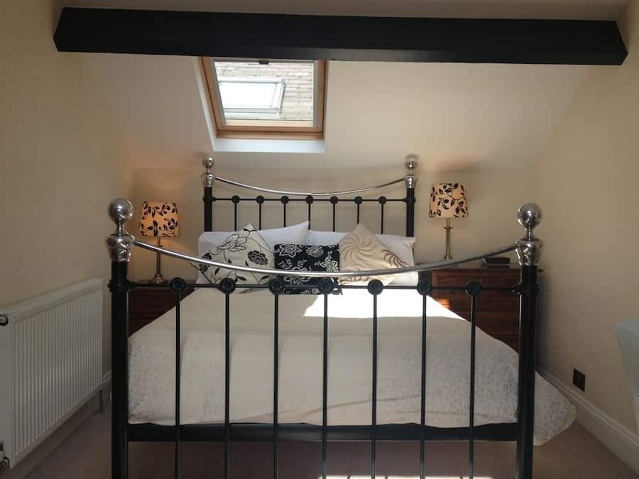 A bedroom with a sloped ceiling, a skylight, a metal bed frame, a white bedspread, two bedside lamps, and a wooden nightstand.