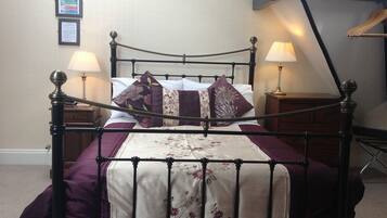 A neatly made bed with a floral bedspread, two bedside lamps, and a framed notice on the wall.