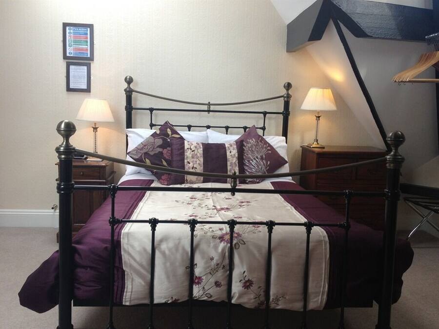 A neatly made bed with a floral bedspread, two bedside lamps, and a framed notice on the wall.