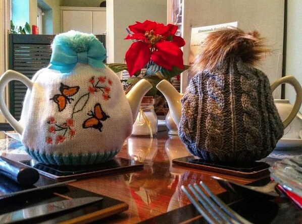 Two knitted teapots with floral designs on a wooden table.