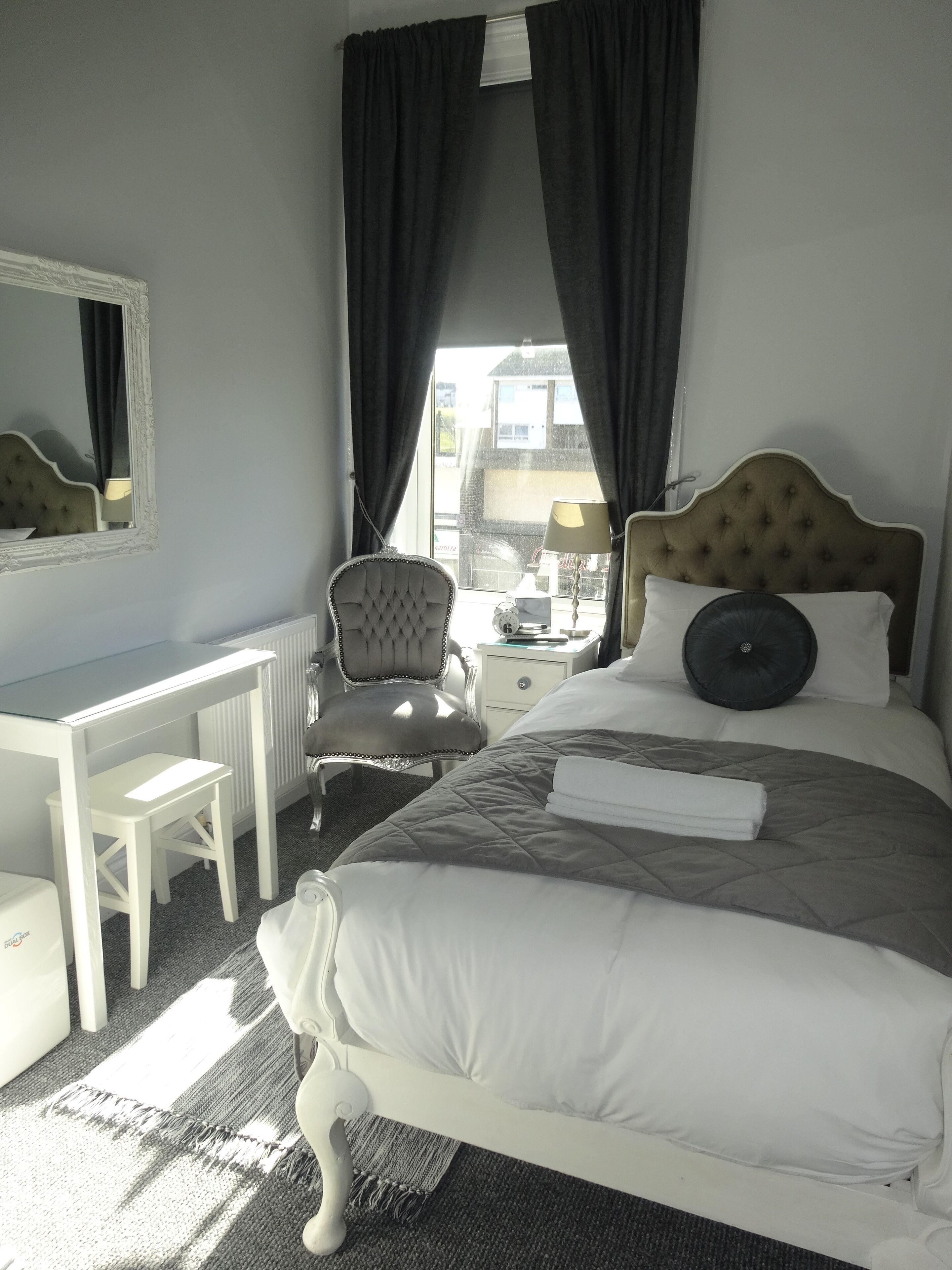 Une chambre d’hôtel avec un lit, un bureau, une chaise et une fenêtre avec des rideaux.