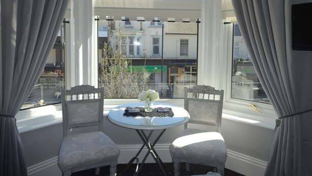 A room with a round table and two chairs, a vase with flowers, and a view of buildings outside.