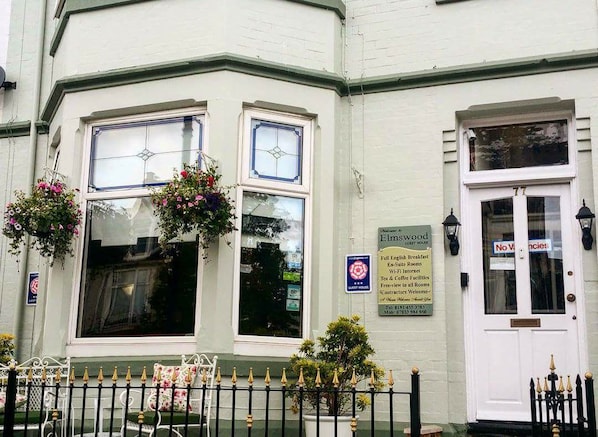 A corner building with a white facade, two windows with blue frames, and a door with a sign stating "No Vacancies." - Elmswood Guest House (South Shields)