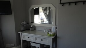 A hotel room with a white desk, a mirror, a small trash bin, and a TV mounted on the wall.