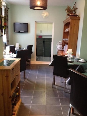 A dining area with a television mounted on the wall, a wooden cabinet with bottles, and a tiled floor. - Elmswood Guest House (South Shields)