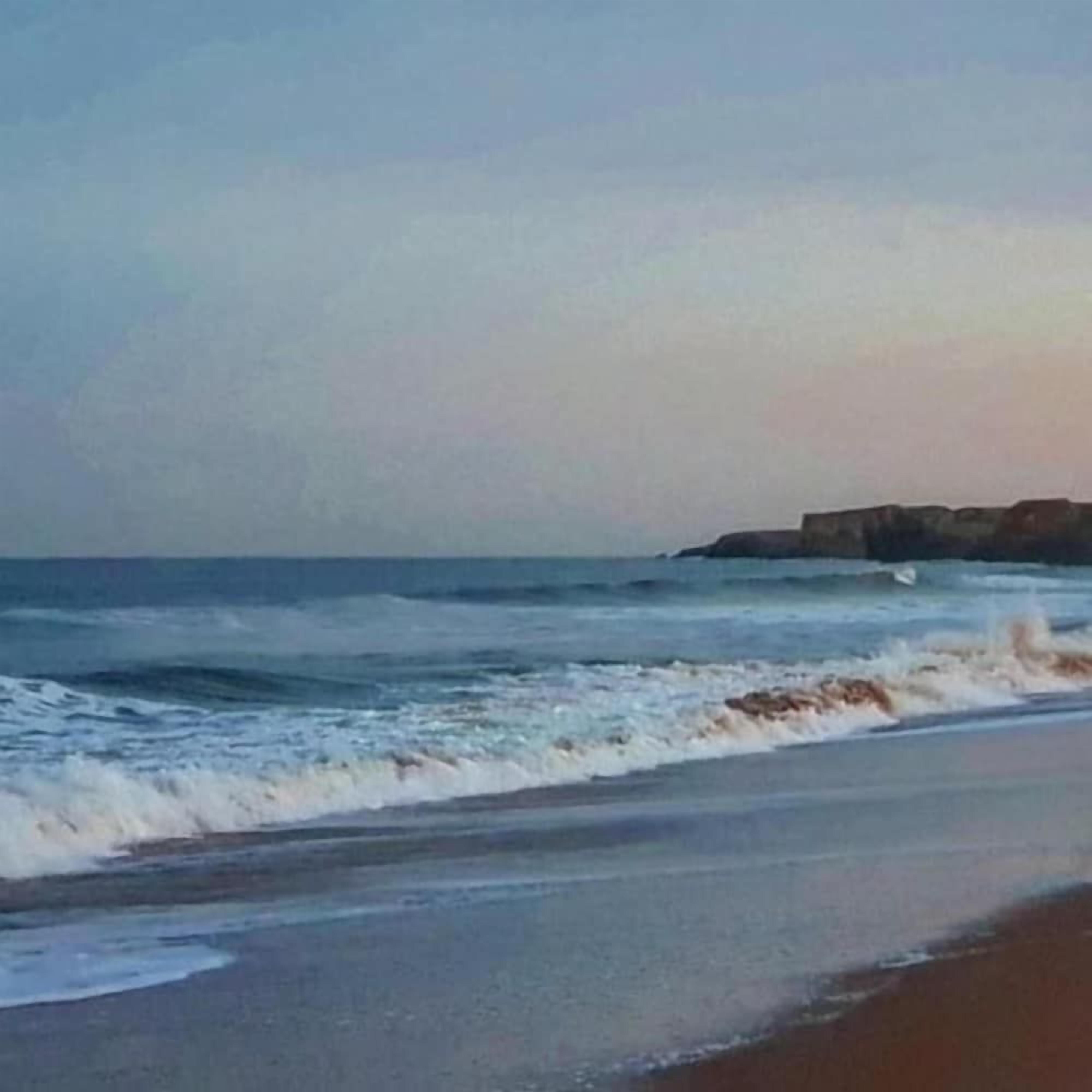 Ein Strand mit Wellen und einer Felsformation in der Ferne.