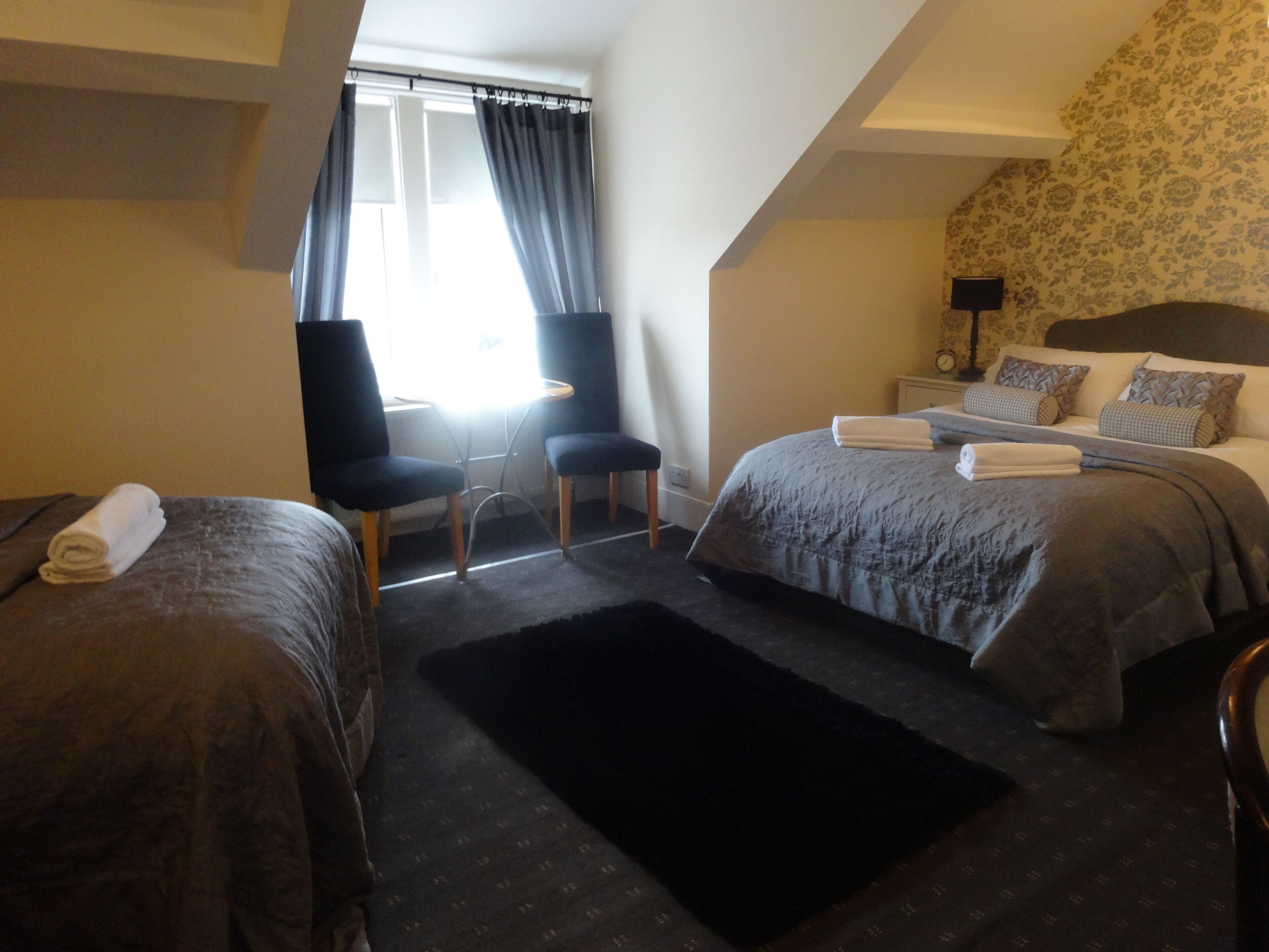 A hotel room with two beds, a desk, chairs, and a window with curtains.