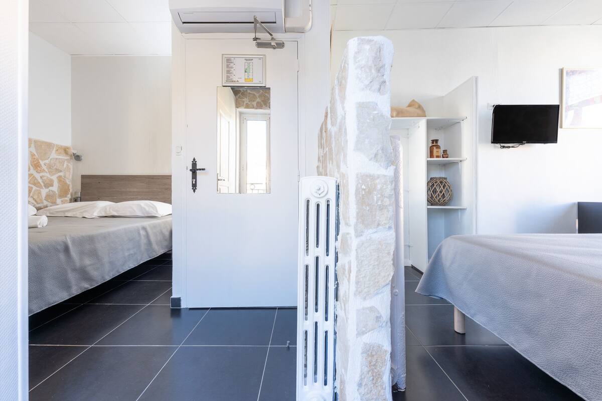 Habitación de hotel con dos camas, un pilar de piedra, una puerta blanca, un televisor montado y un estante con objetos.