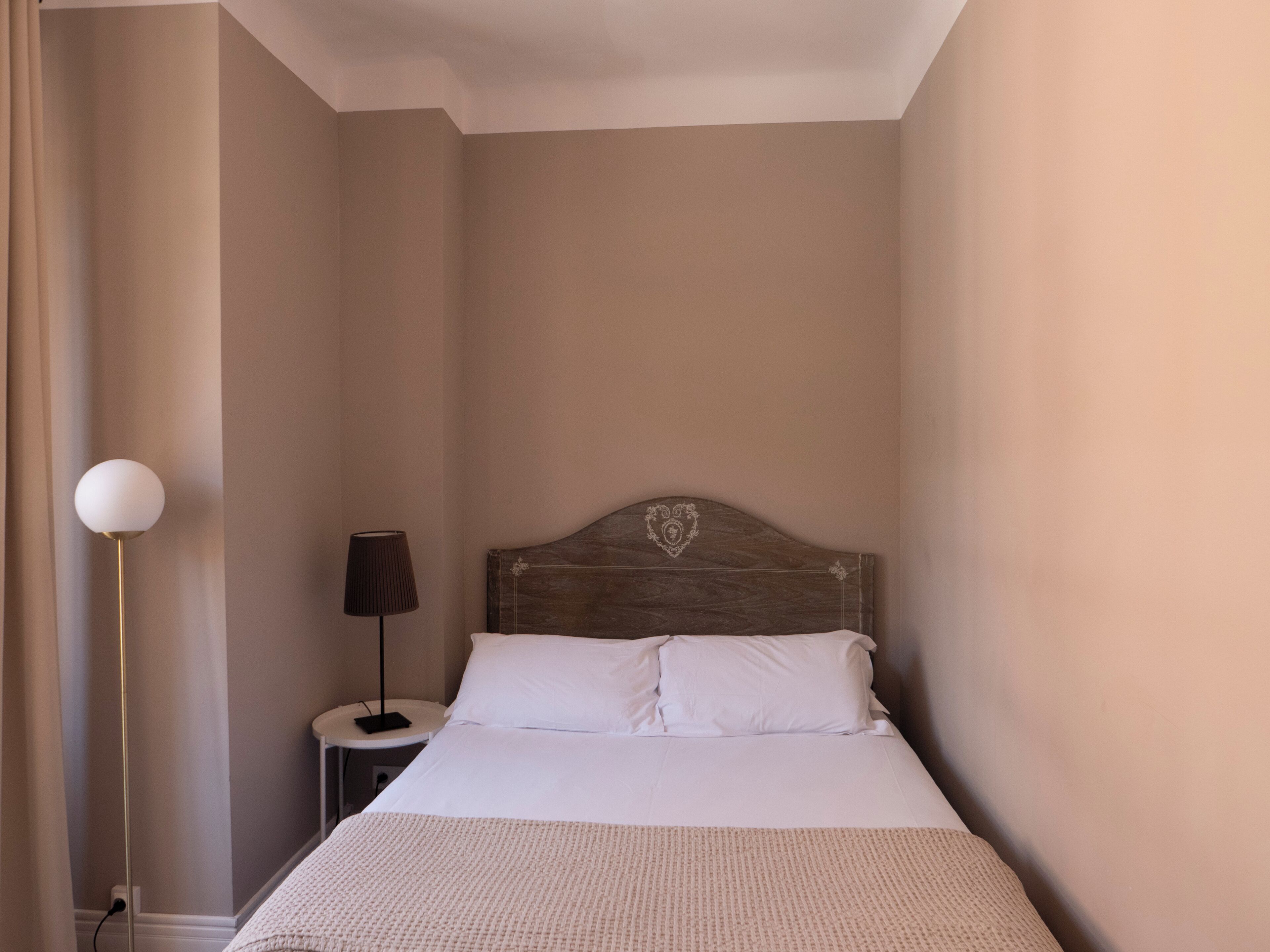 A bedroom with a single bed, a bedside table, a lamp, and a wall-mounted light fixture.