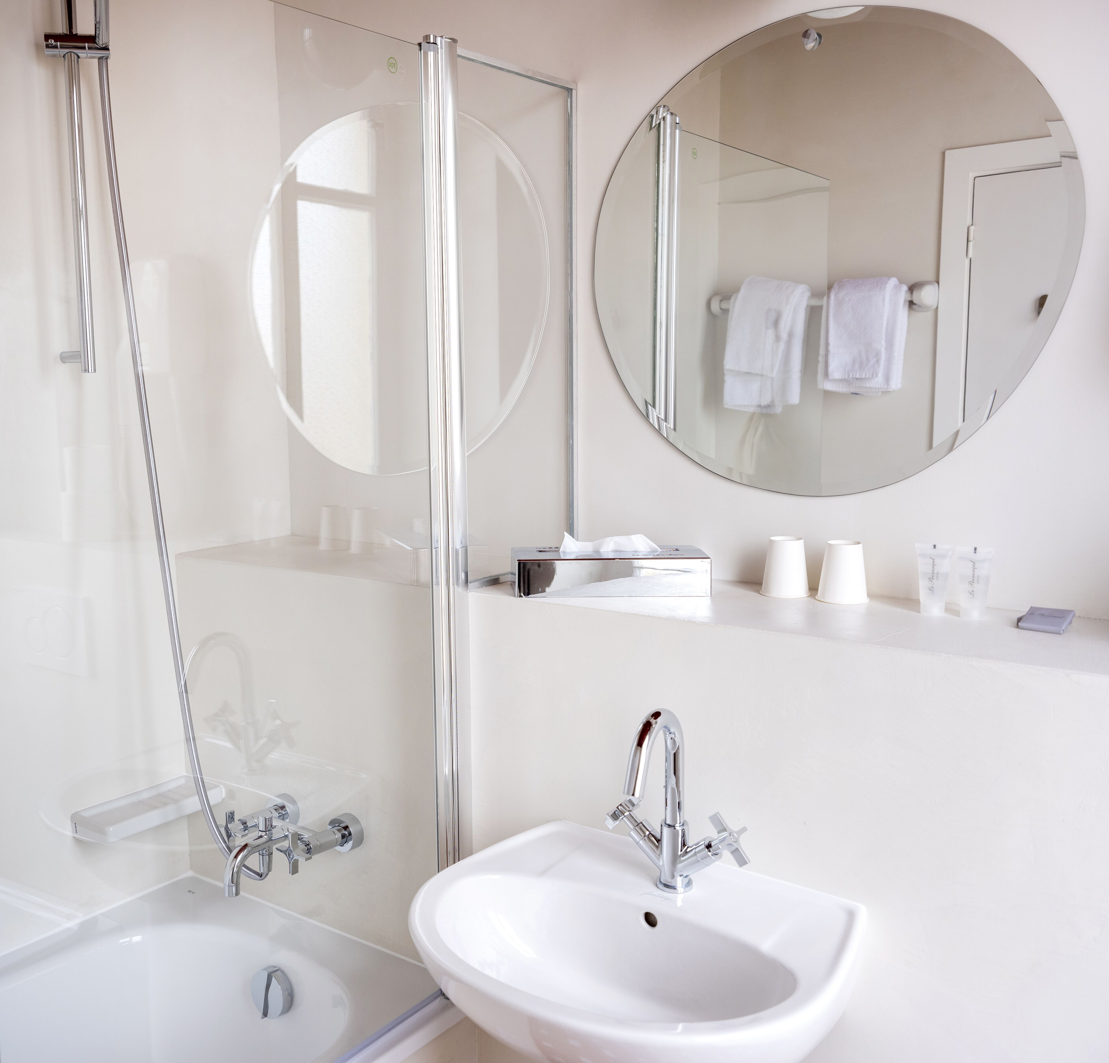 Un bagno moderno con doccia vetrata, uno specchio rotondo, un lavandino e articoli da toilette sul ripiano.