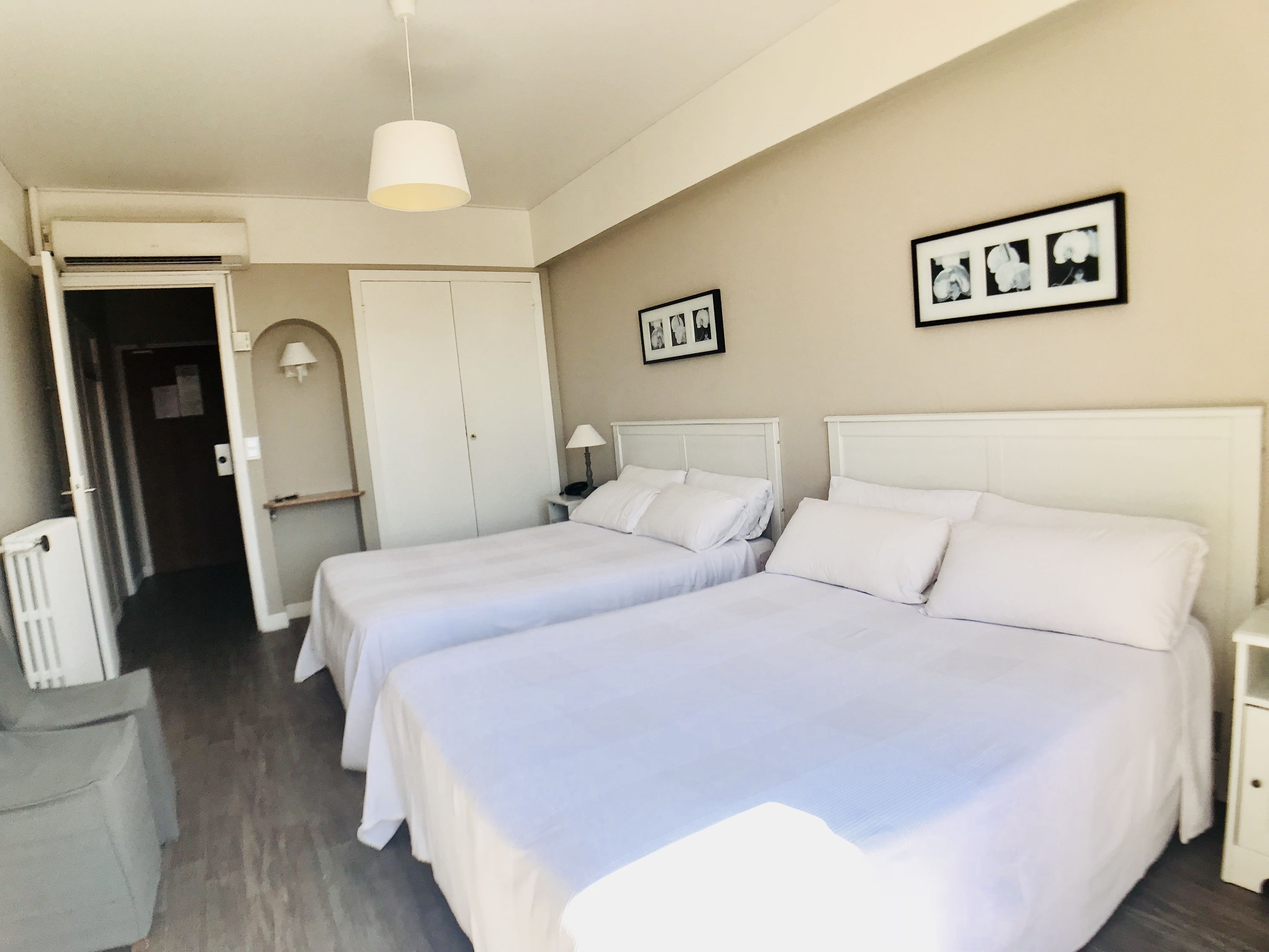 Une chambre d’hôtel avec deux lits, une petite table, une chaise, une porte et un tableau accroché au mur.